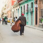 Old Havana - man carrying stringed instrument while walking the pavement during daytime